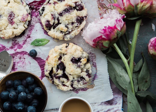 blueberry scones on parchment surrounded by a bowl of berries and large flowers